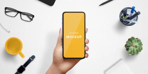 Smart Phone In Woman Hand Mockup, Above Work Desk. Top View, Flat Lay Composition Premium PSD