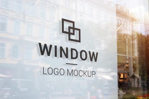 Black Logo Mockup On Store Window With White Indoor. Modern Street Shop Window In The City Center. Buildings And Sun Light In Reflection Premium PSD
