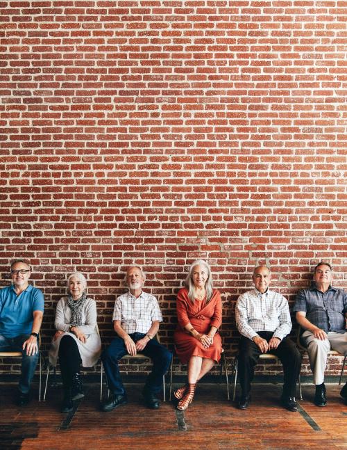 Diverse elderly people sitting in a row against a brick wall background - 2027833