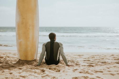 Black man sitting by his surfboard - 1079865