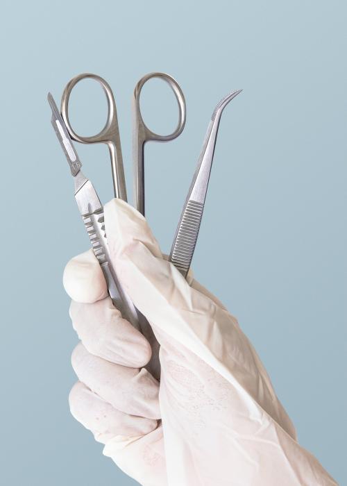 Gloved hand holding stainless steel medical instruments - 2054339