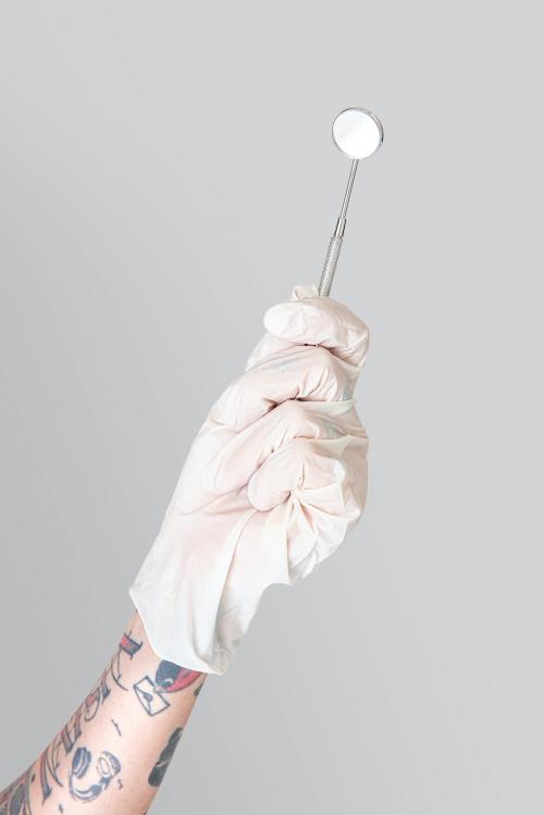 Tattooed hand in a white glove holding a dentist's mirror mockup - 2054360