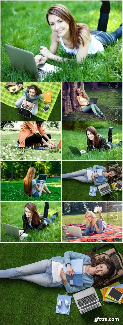 Girls with laptop lie on green grass stock photo